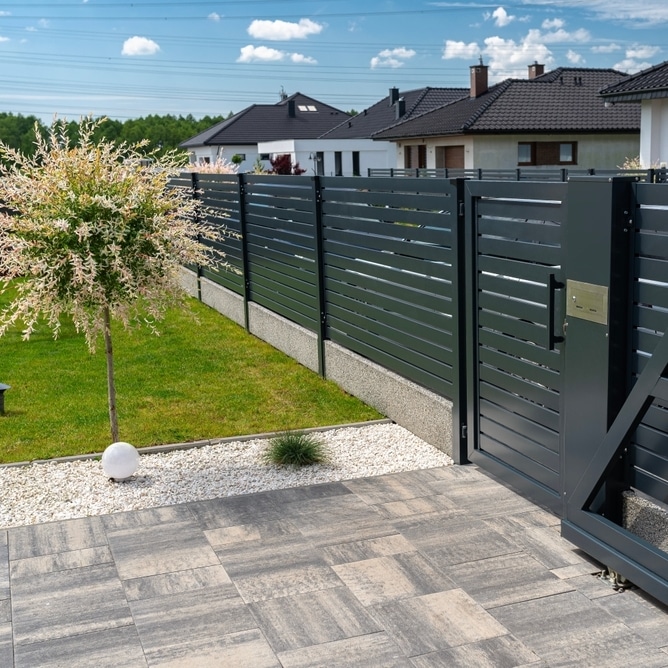 Clôture en aluminium gris anthracite à lames horizontales et portillon moderne dans un jardin paysagé.